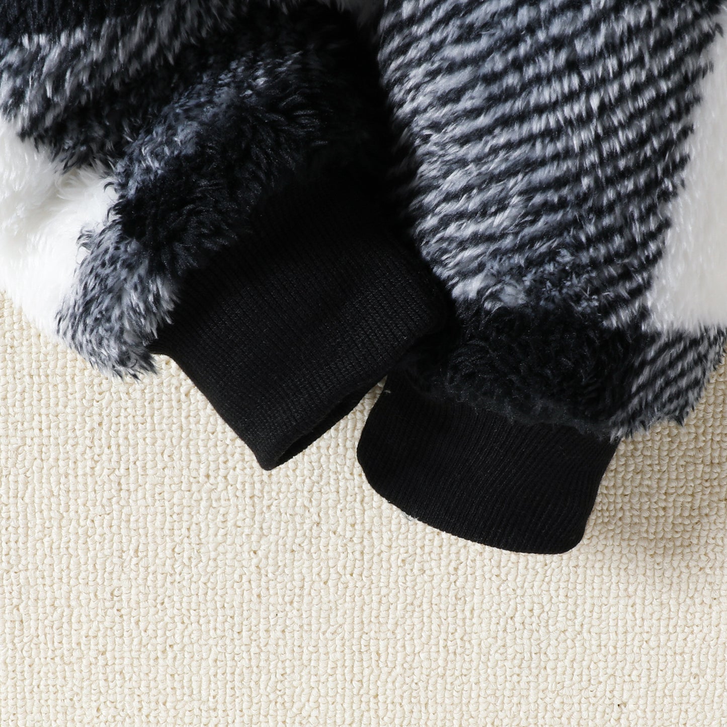 Close-up of a black and gray textured garment with ribbed cuffs on a beige fabric background.