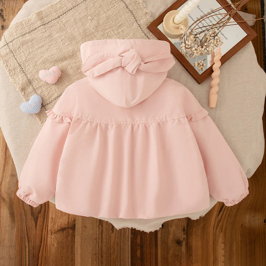 Pink children's coat with a bow on a wooden floor