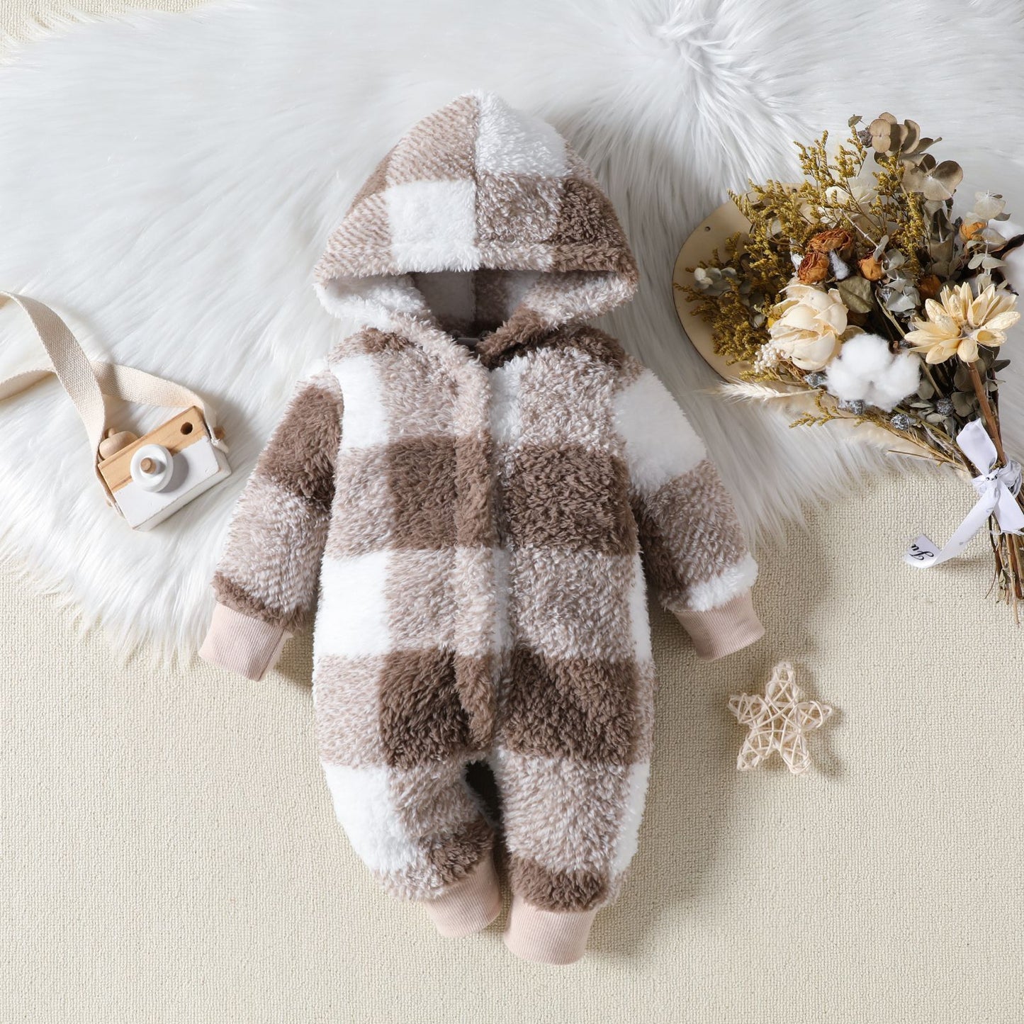 Plaid baby onesie with a hood on a soft surface with decorative elements.