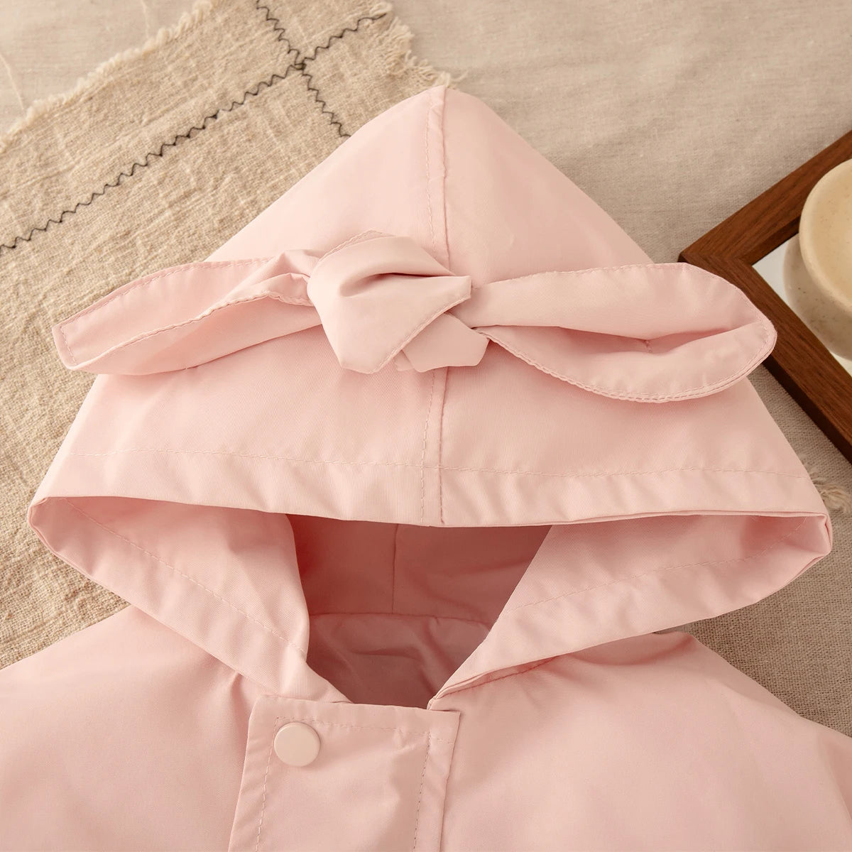 Pink hooded coat with a large bow on a textured surface