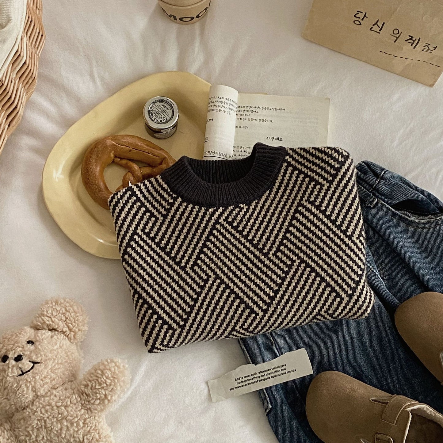 Textured black and beige bag on a white surface with a teddy bear, book, and other items.