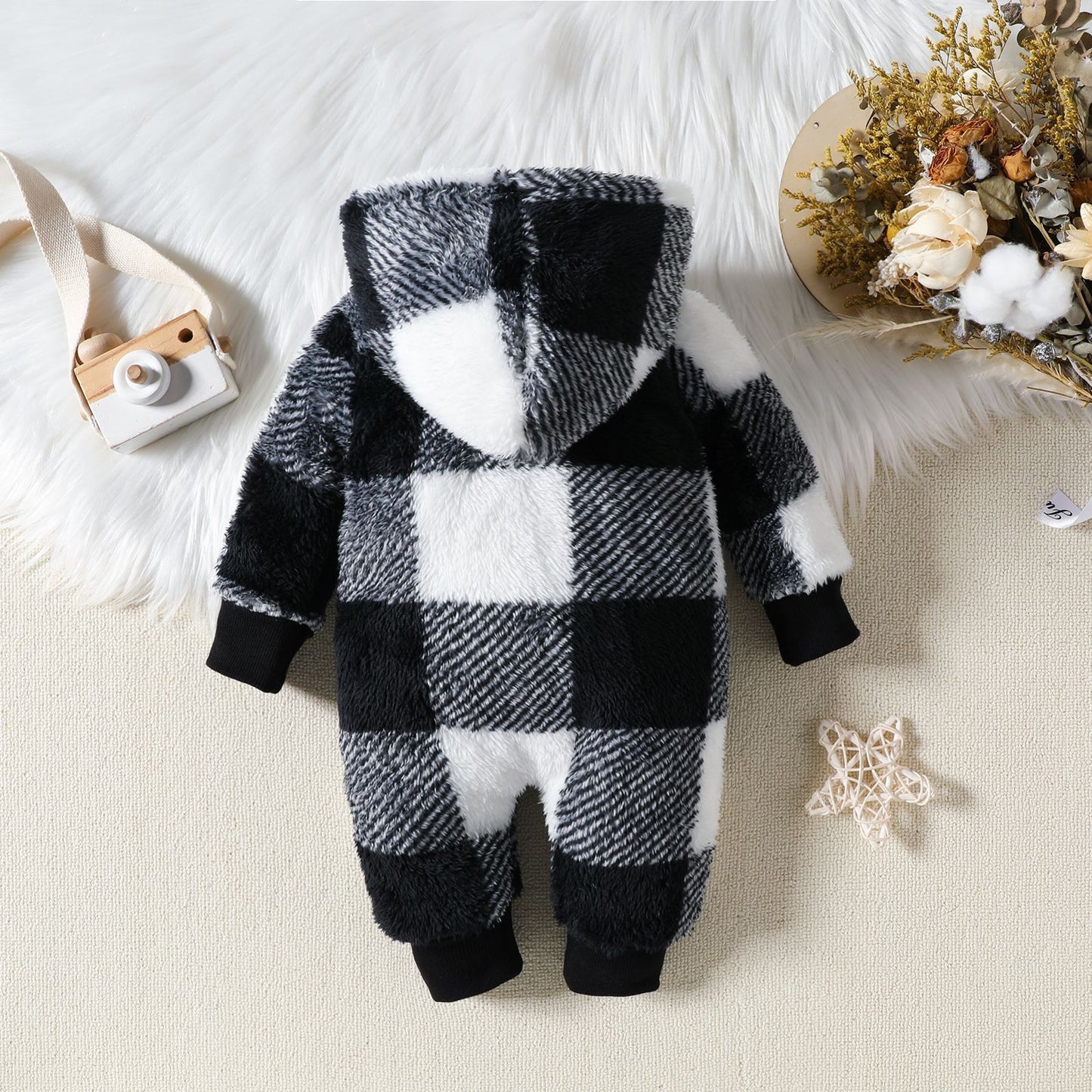 Black and white checkered baby onesie on a soft surface with decorative items.