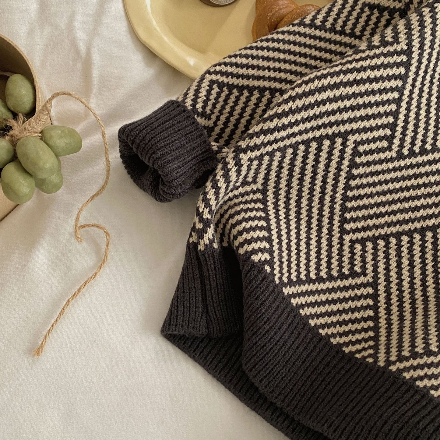 Black and white patterned sweater on a light surface with a small plant.