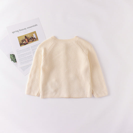 Beige baby sweater on a white background with a magazine underneath