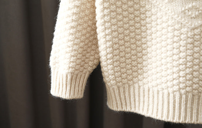 Close-up of a textured beige sweater against a dark background