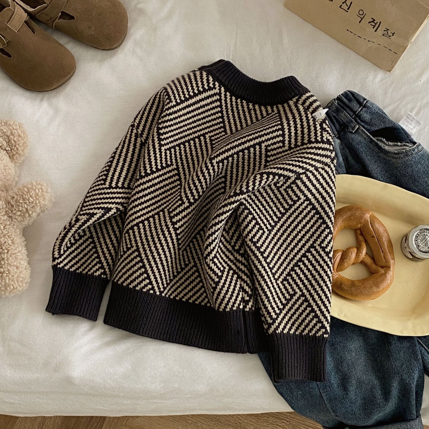 Black and white patterned sweater on a textured surface with shoes, jeans, and a bagel in the background.