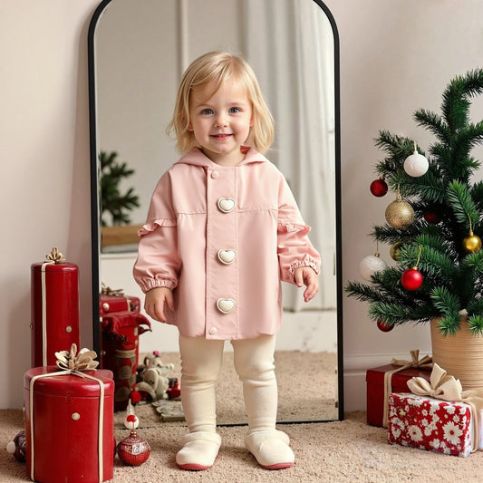 Child in a pink coat standing in a festive room with Christmas decorations.