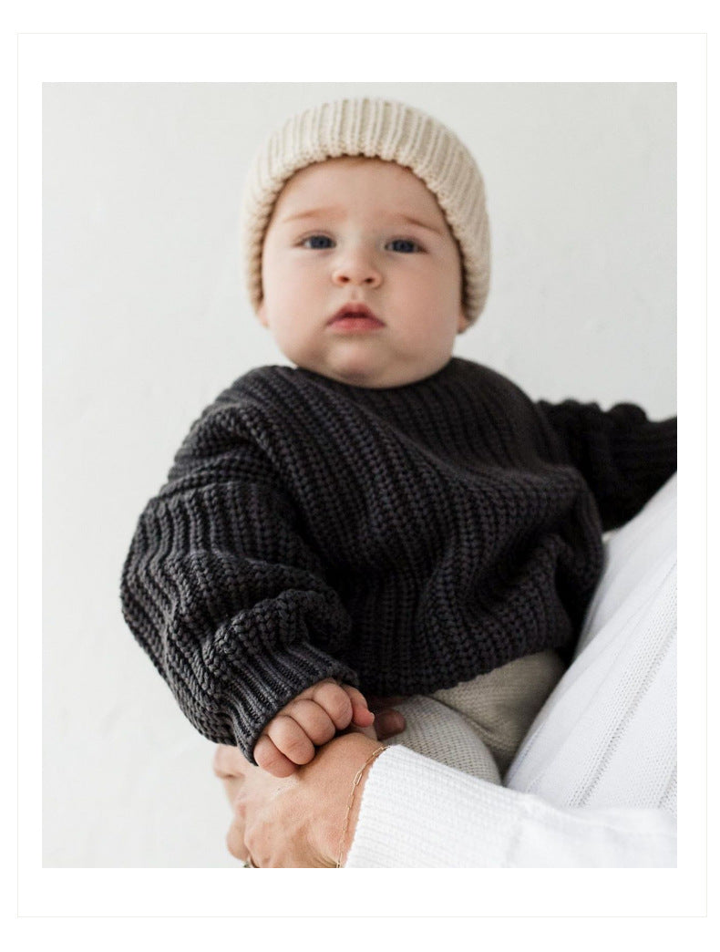 Baby wearing a dark sweater and beige knit hat on a white background