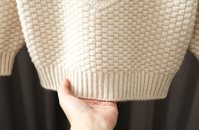 Close-up of a beige knitted sweater held by a hand against a dark background