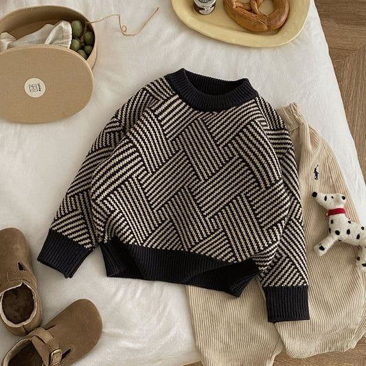 Herringbone patterned sweater on a white surface with shoes and a toy in the background