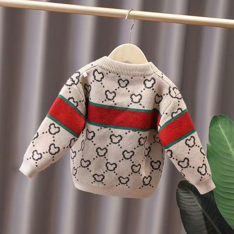 Children's sweater with heart pattern and red sleeves on a hanger against a neutral background