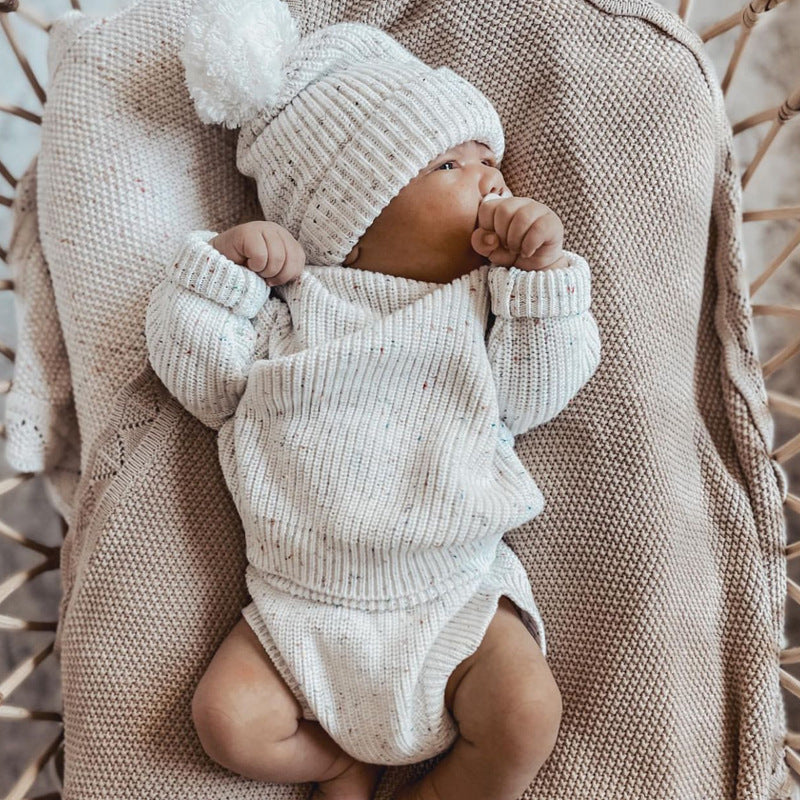 Baby in a knitted outfit and hat lying on a textured surface