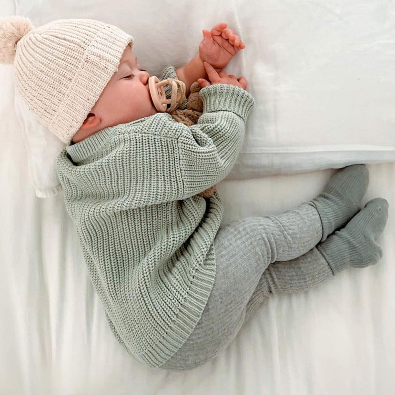 Newborn baby wrapped in a green blanket and wearing a beige knit hat on a white surface.