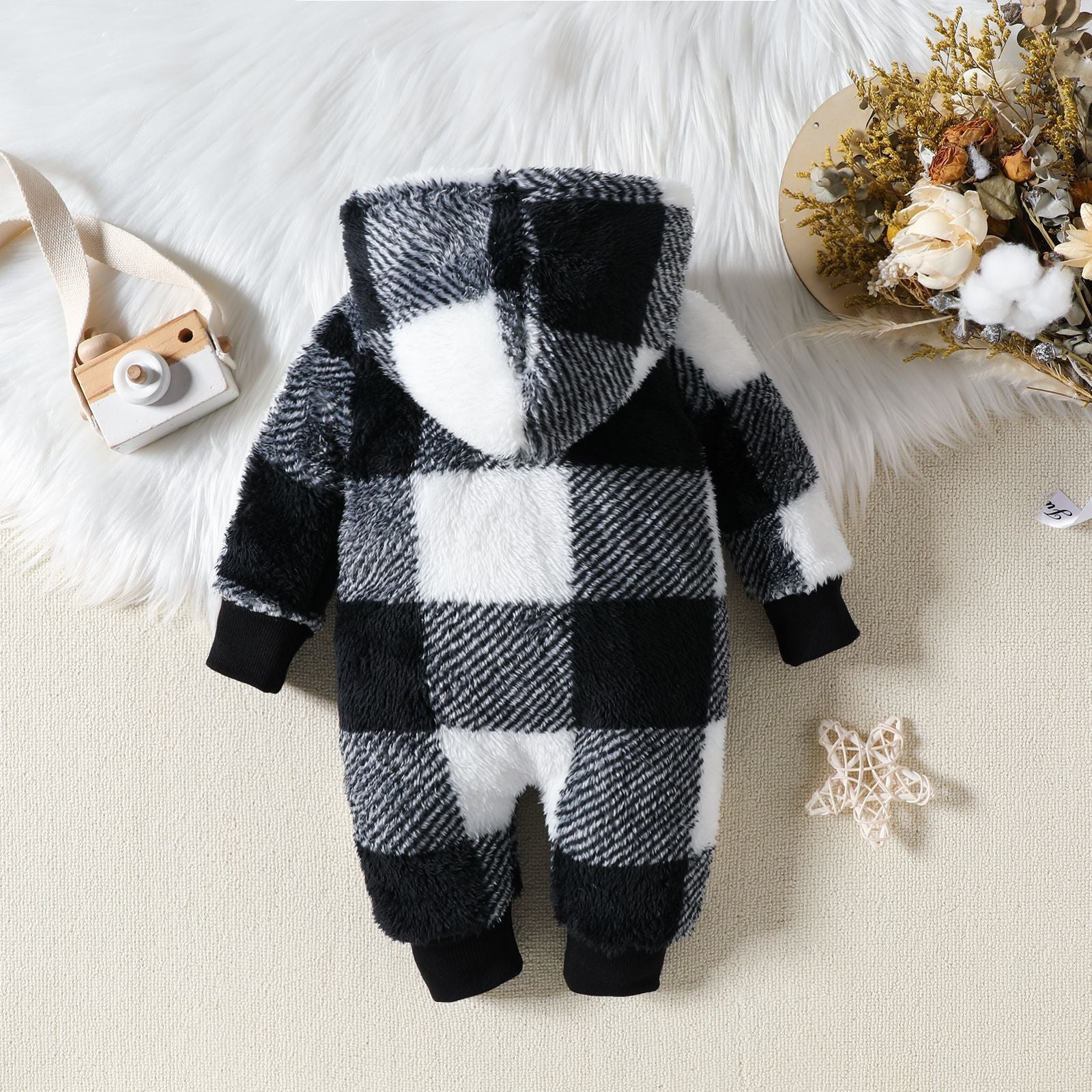 Black and white checkered baby onesie on a soft surface with decorative items.