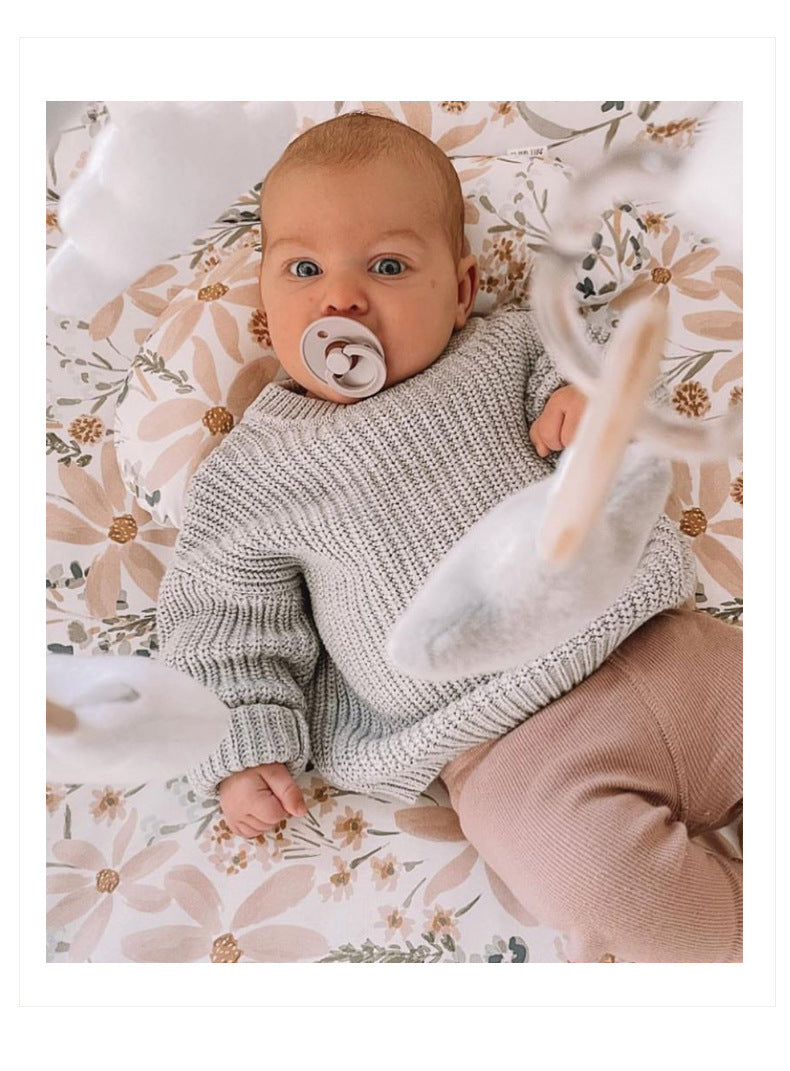 Baby wearing a knitted sweater and holding a toy on a floral blanket