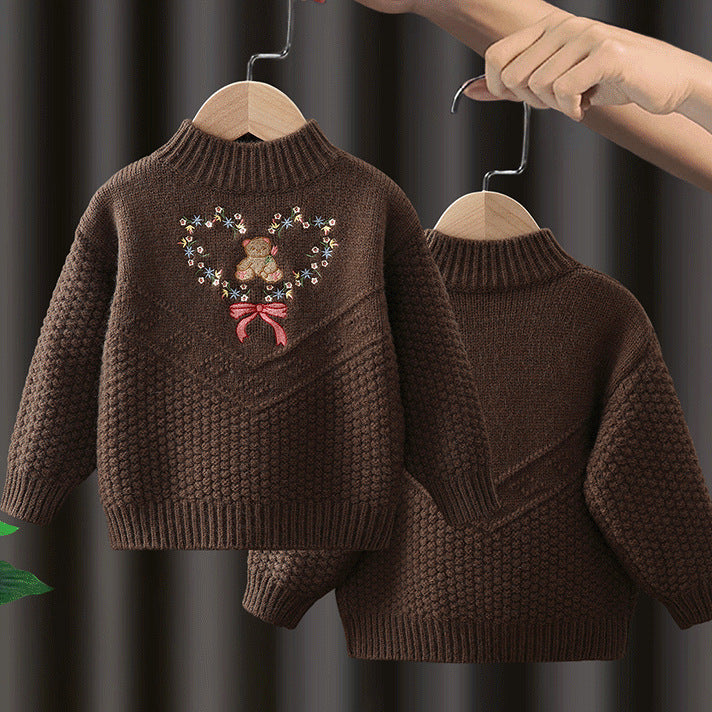 Brown knitted sweater with teddy bear design on a hanger against a dark background