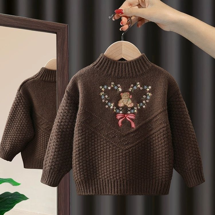 Brown knitted sweater with teddy bear design on a hanger against a dark background