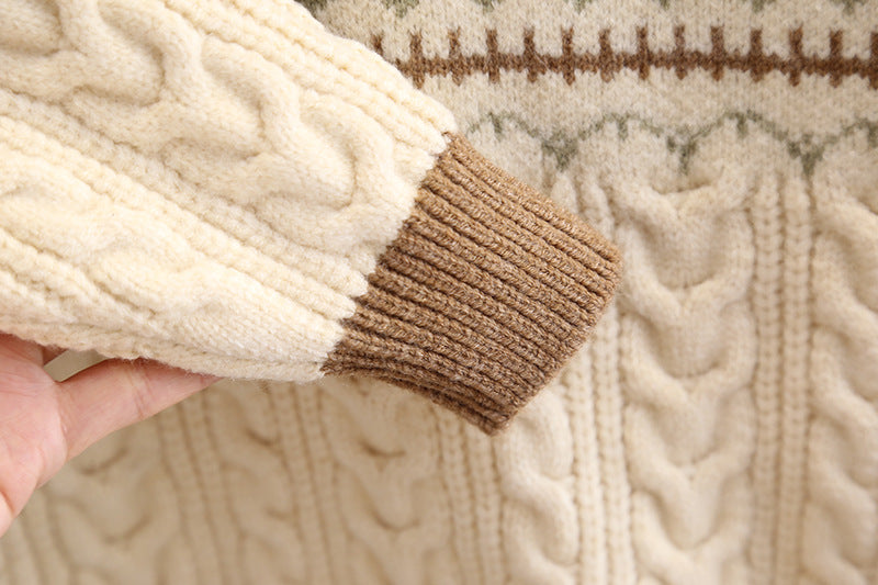 Close-up of a cable-knit sweater sleeve with a brown accent held by a hand.