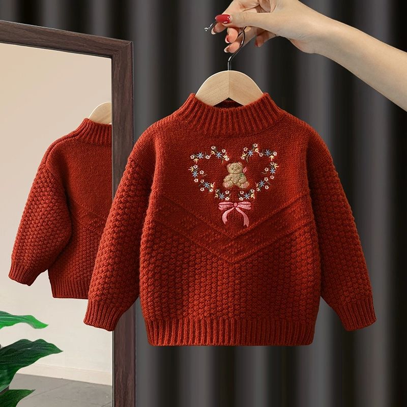 Red knitted sweater with a teddy bear design on a hanger against a dark background.