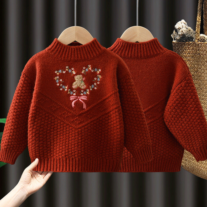 Red knitted sweater with a heart design featuring a teddy bear on a hanger against a dark background.
