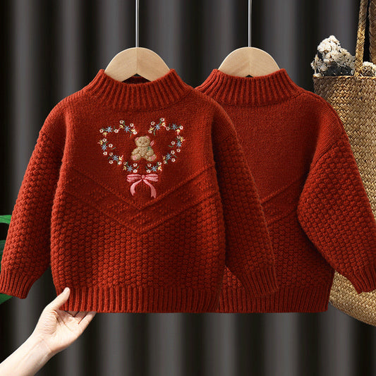 Red knitted sweater with a heart design featuring a teddy bear on a hanger against a dark background.