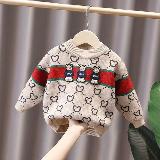 Children's sweater with bear design and colorful stripes on a hanger against a neutral background
