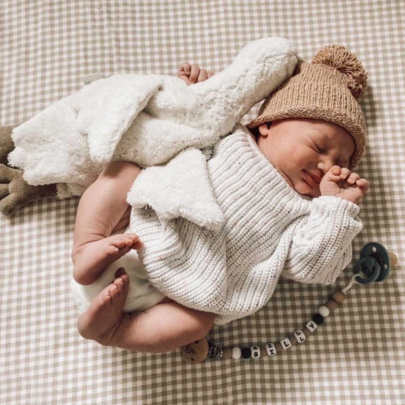 Newborn baby wrapped in a white blanket and wearing a knitted outfit on a checkered surface.