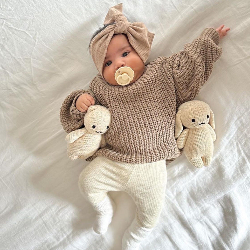Baby in beige knitted outfit with plush toys on a white blanket