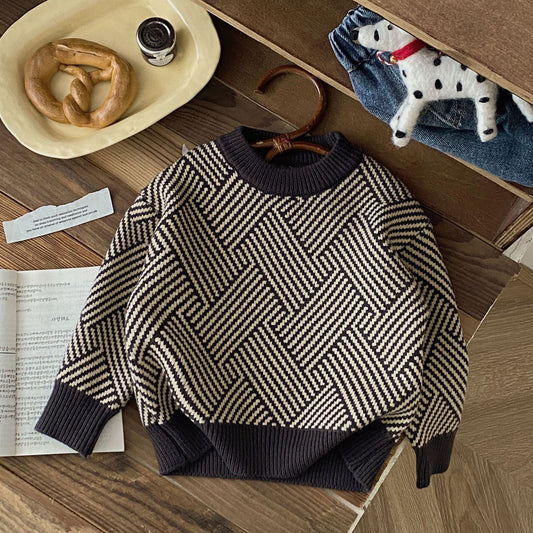 Children's herringbone sweater on a wooden surface with a pretzel and coffee cup in the background.
